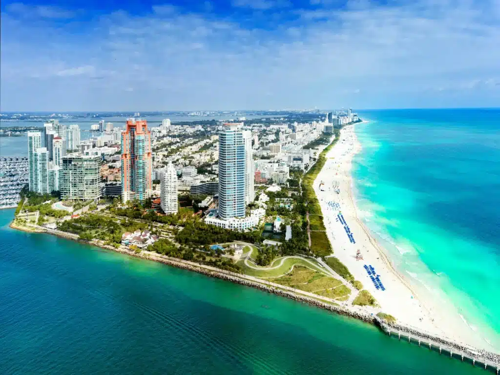 Aerial view of a coastal city with tall buildings, green parks, and a long sandy beach beside turquoise waters.